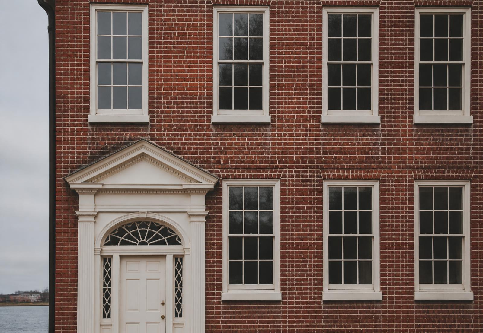 Red brick façade with a white pedimented doorway, arched fanlight and twelve-over-twelve sash windows